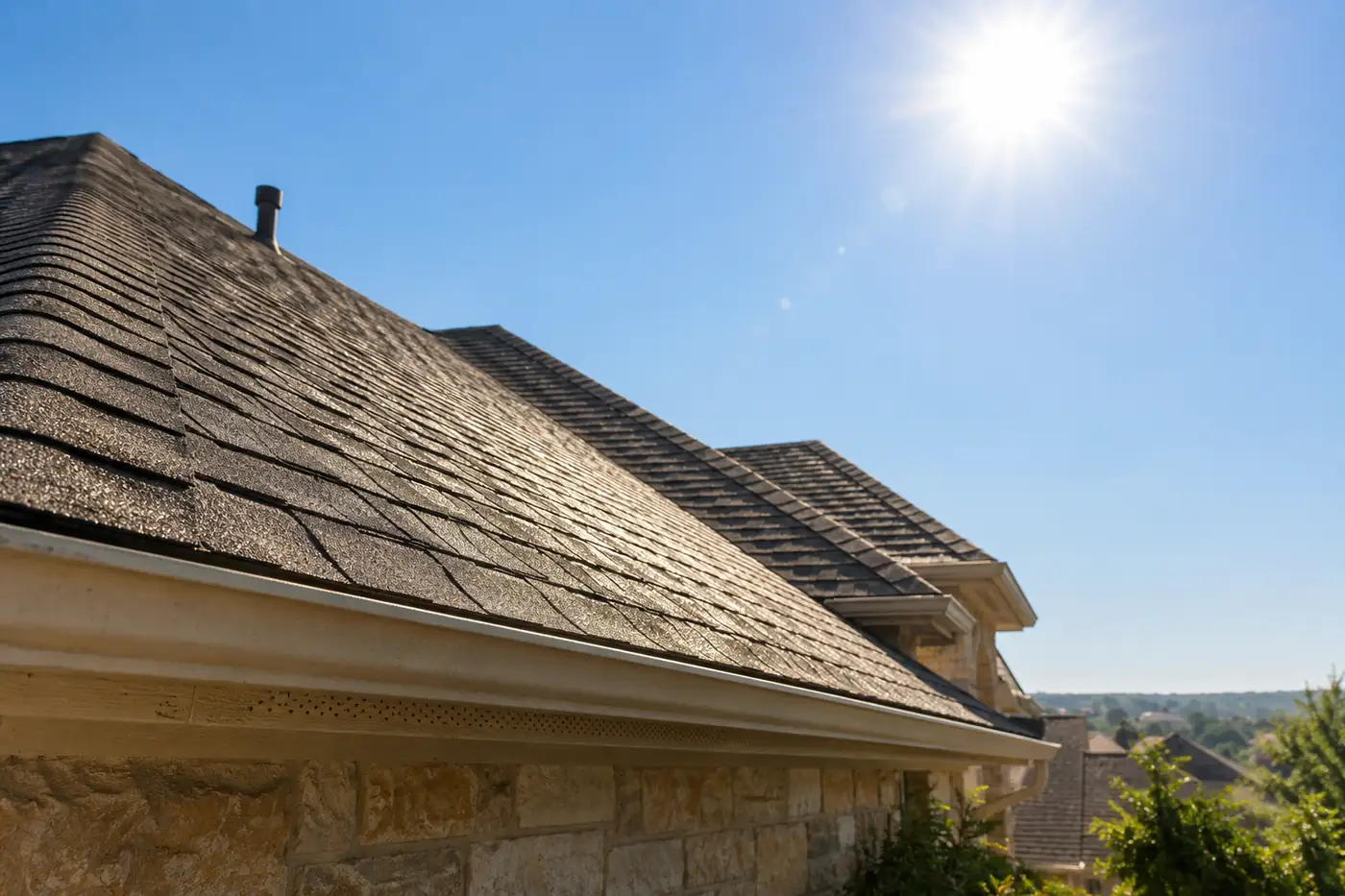 Asphalt shingle roof under an intense white summer sun, seen from the eave