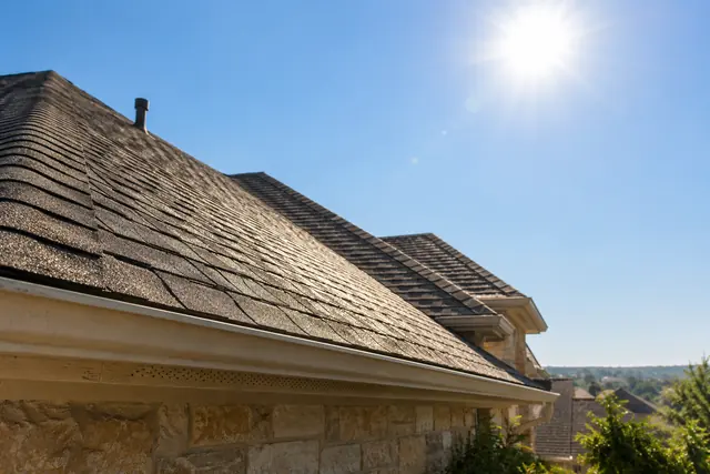 Asphalt shingle roof under an intense white summer sun, seen from the eave